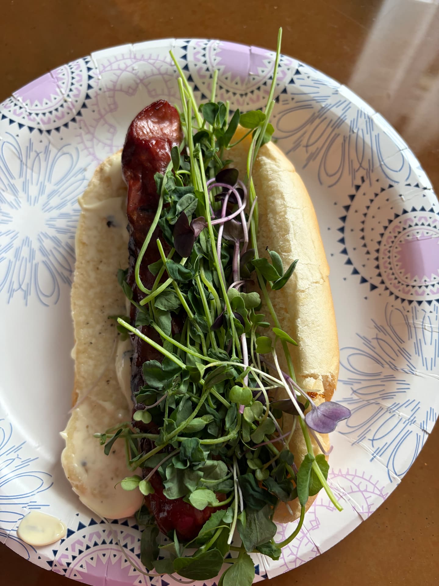 Polish sausage in a soft bun topped with radish and field pea microgreens on a patterned paper plate