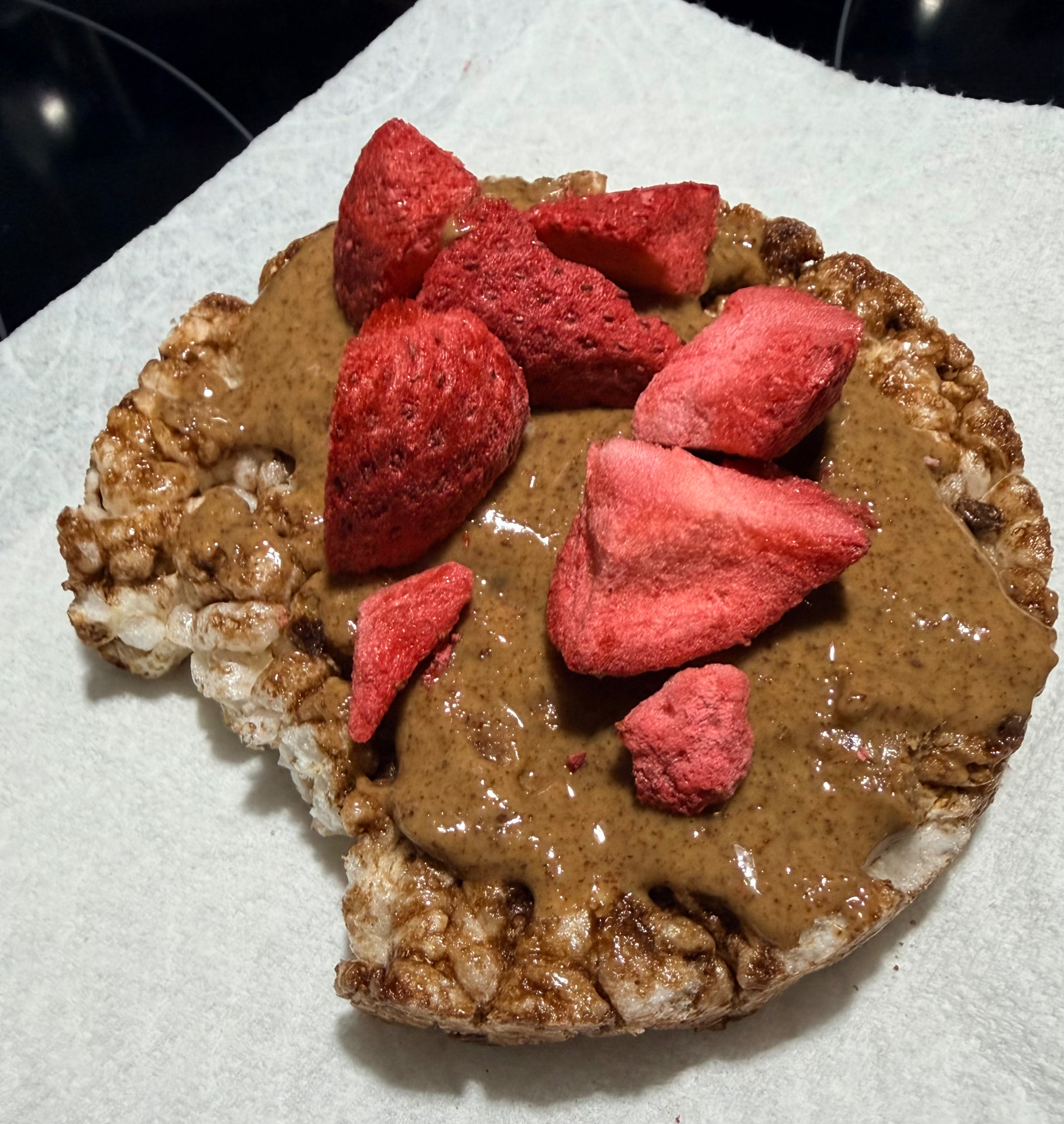 Chocolate rice cake spread with almond butter and topped with freeze-dried strawberries on a white paper towel