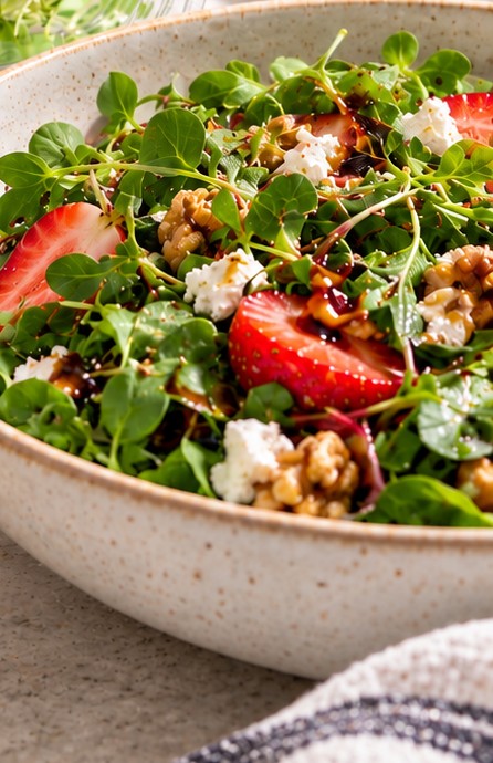 Bowl of microgreen salad with sliced strawberries, walnuts, goat cheese, and balsamic glaze