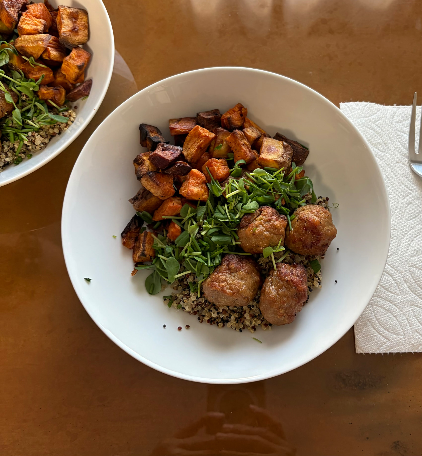 White bowl filled with quinoa, chicken meatballs, roasted sweet potatoes, and field pea microgreens