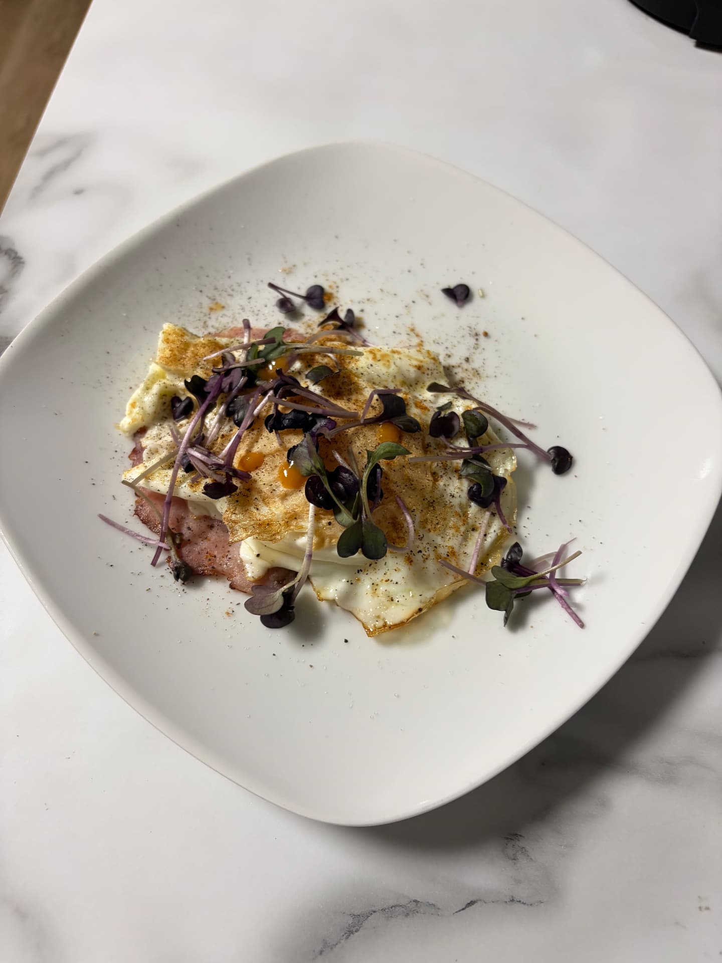 Fried eggs and ham on a white plate topped with radish microgreens, salt, and pepper